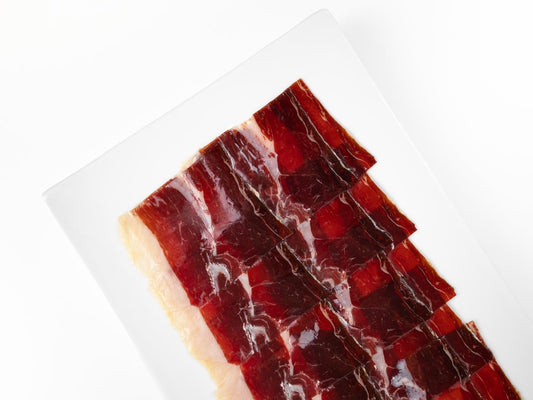 Rebanada de jamón Gran Reserva de 80g de la marca MONJAMON Y MAS, cortada a cuchillo, en plato blanco.