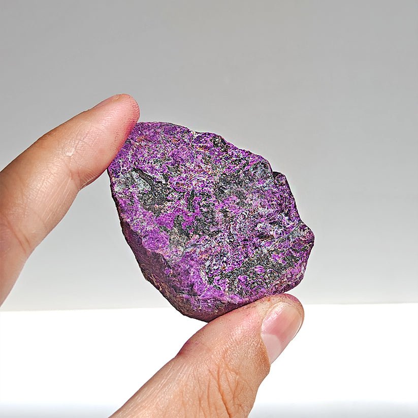 Cristal de purpurita en bruto, gema natural sin pulir, de la marca Mystical Tienda, muestra su forma irregular y color violeta.