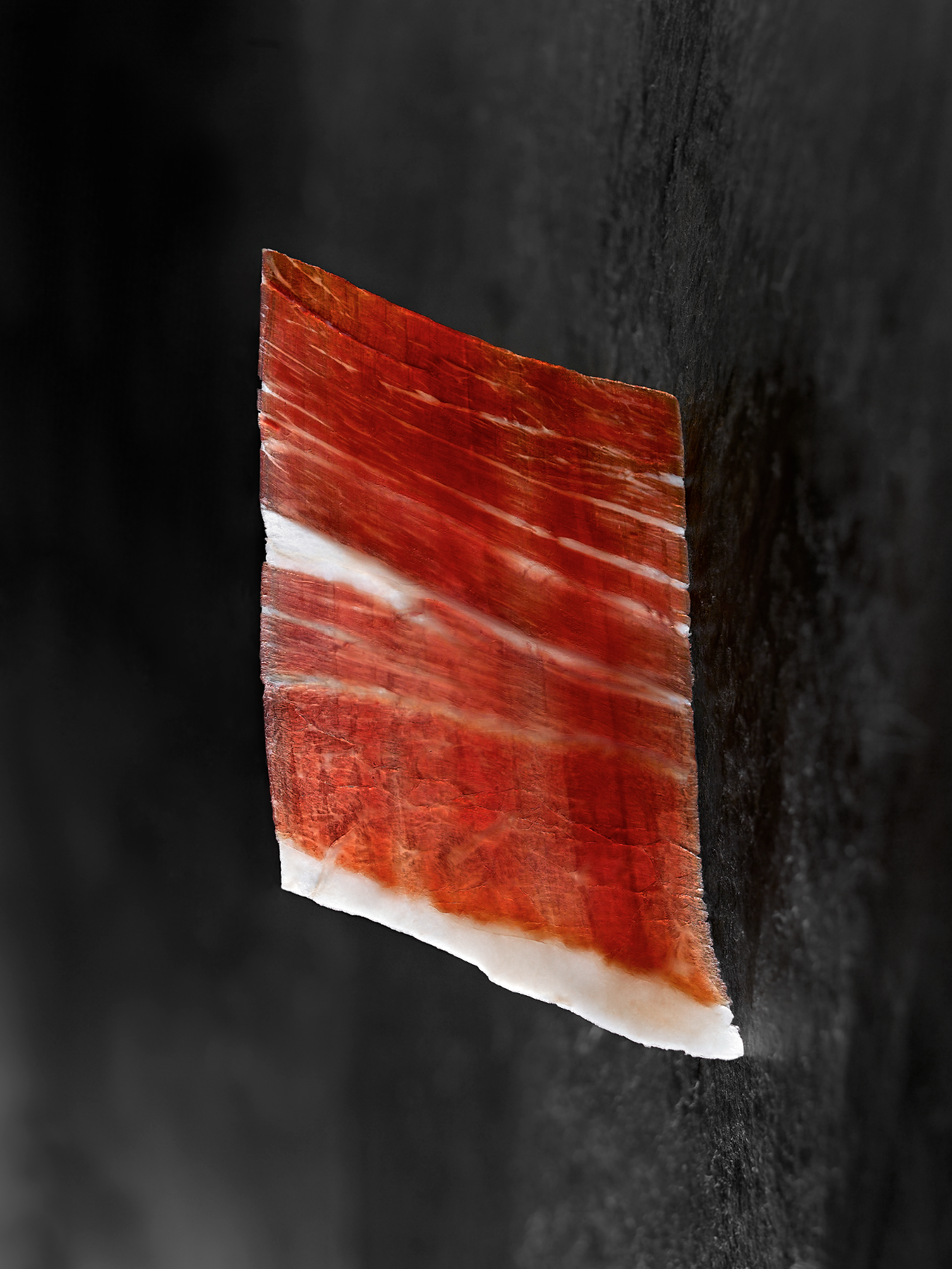 Jamón de Bellota 100% Ibérico de la marca MONJAMON Y MAS, en lonchas finas sobre fondo blanco.