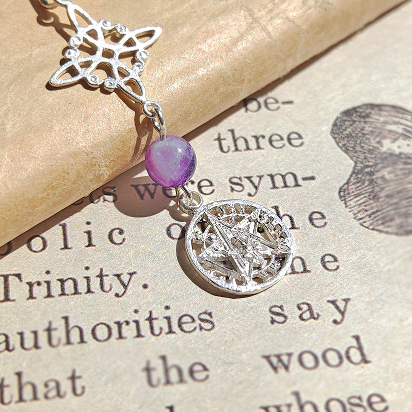 Colgante de plata con nudo de bruja, símbolo tetragramaton y bola de amatista en color morado, estilo místico y elegante.