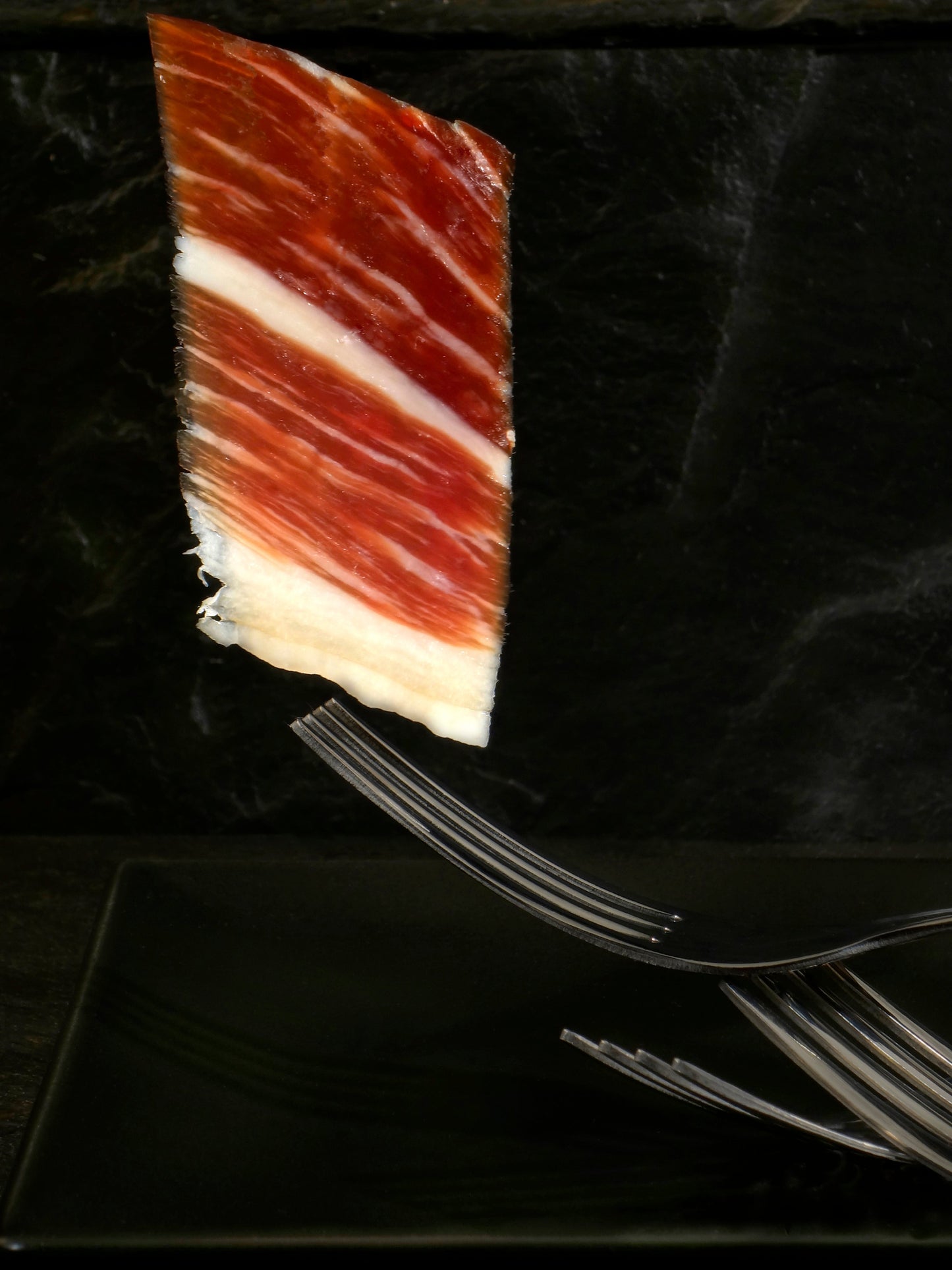 Jamón de Bellota 100% Ibérico MONJAMON Y MAS, corte en lonchas finas, con textura y grasa intramuscular visible.