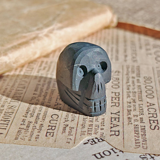 Figura geométrica de calavera de shungit de la marca Mystical Tienda, muestra detalles de la piedra negra y formas esculpidas.