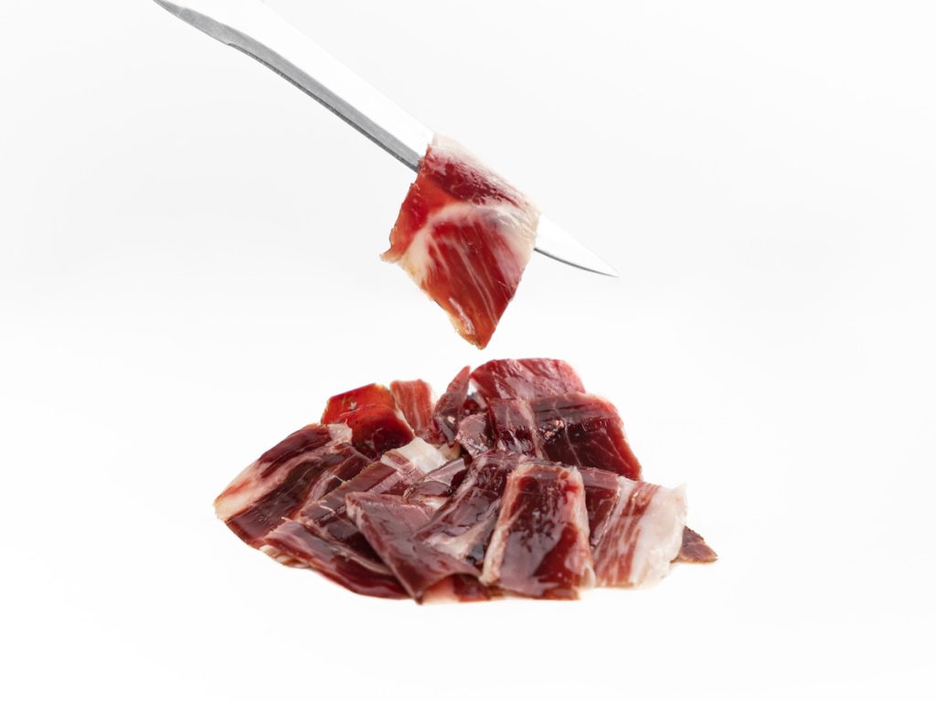 Jamon ibérico Sagrada Paleta de Bellota 100% Ibérica cortado en loncha con cuchillo, presentado en una tabla.