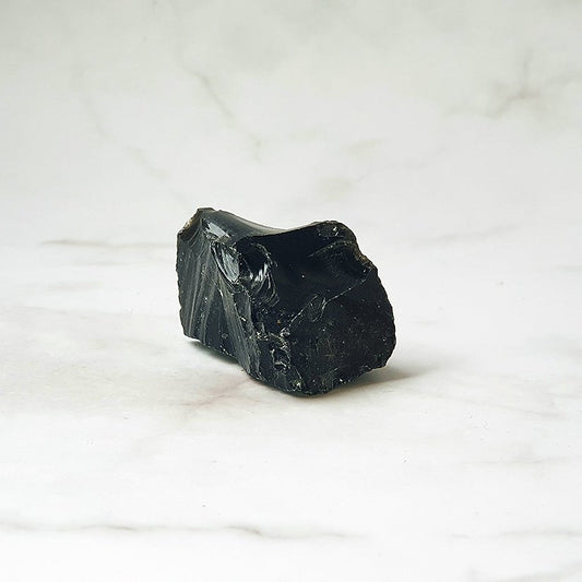 Pedazo de obsidiana en bruto de Mystical Tienda, con superficie natural y color negro brillante, muestra su forma irregular y textura rugosa.