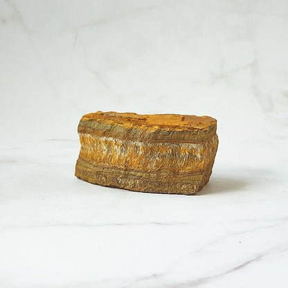 Ángulo de un ojo de tigre en bruto con vetas doradas y marrones, mostrando su textura natural y forma irregular.
