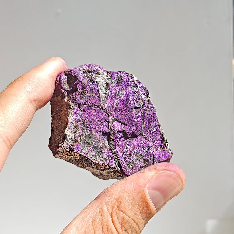 Cristal de purpurita en bruto, mineral natural sin pulir, de color violeta, sobre fondo neutro.