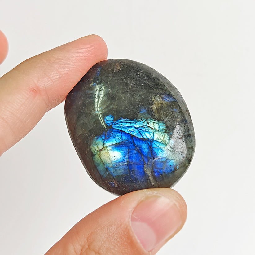 Rodado Palm Stone de labradorita, piedra de energía, con brillo iridiscente, en un fondo neutro, de la marca Mystical Tienda.