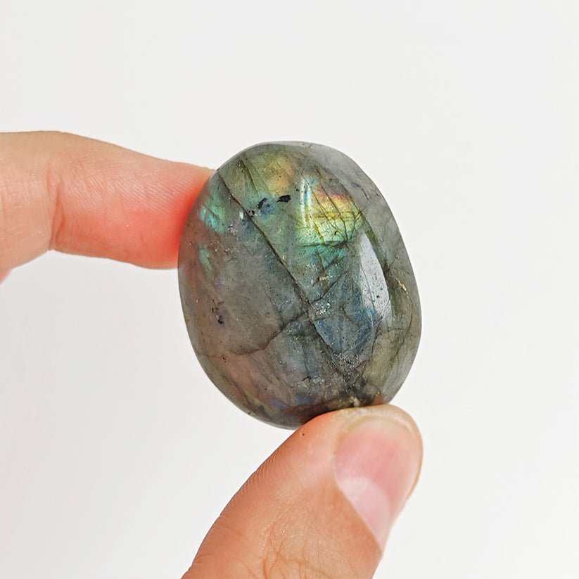 Rodado palm stone de labradorita de Mystical Tienda, piedra pulida y redonda con reflejos azules y verdes en la superficie.